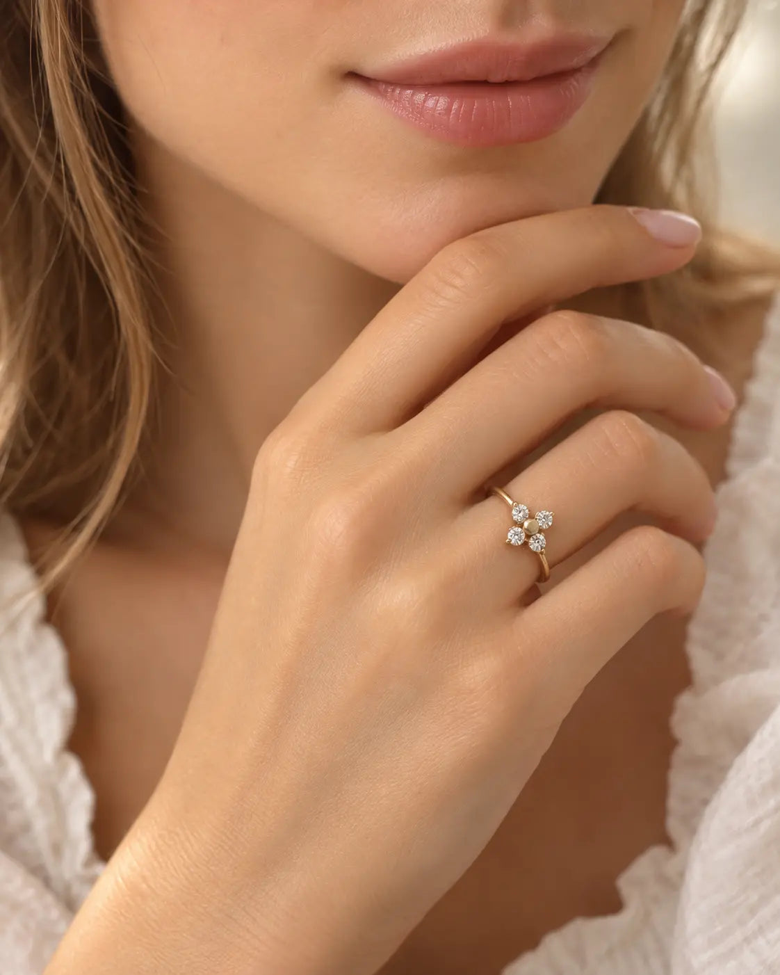 Nahaufnahme des goldenen Elina Zirkonia Blumenrings an einer Hand unter dem Kinn einer Frau