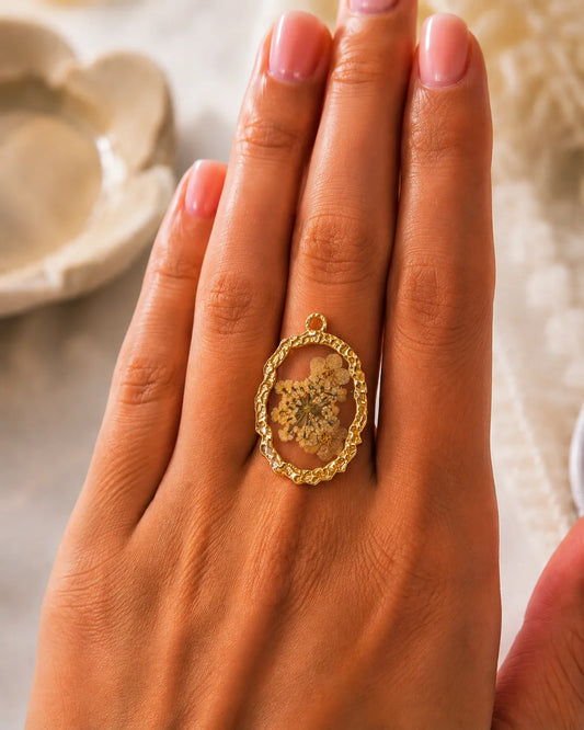 Ovaler, goldener Anhänger aus 18K vergoldetem Titanstahl mit einem gehämmerten Rahmen und einem klaren Acryl-Zentrum, in das echte, weiße Trockenblumen eingebettet sind, ideal für personalisierbare Armbänder und Ketten