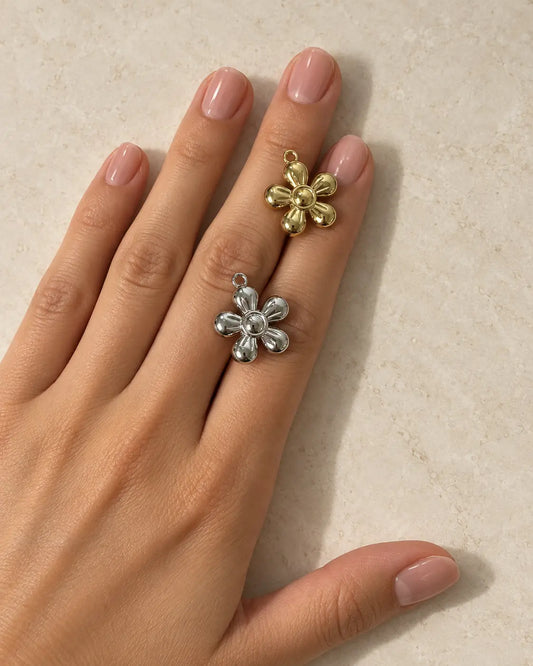 Goldener und silberfarbener Flora Blumen Charm auf einer Hand vor hellem Steinhintergrund
