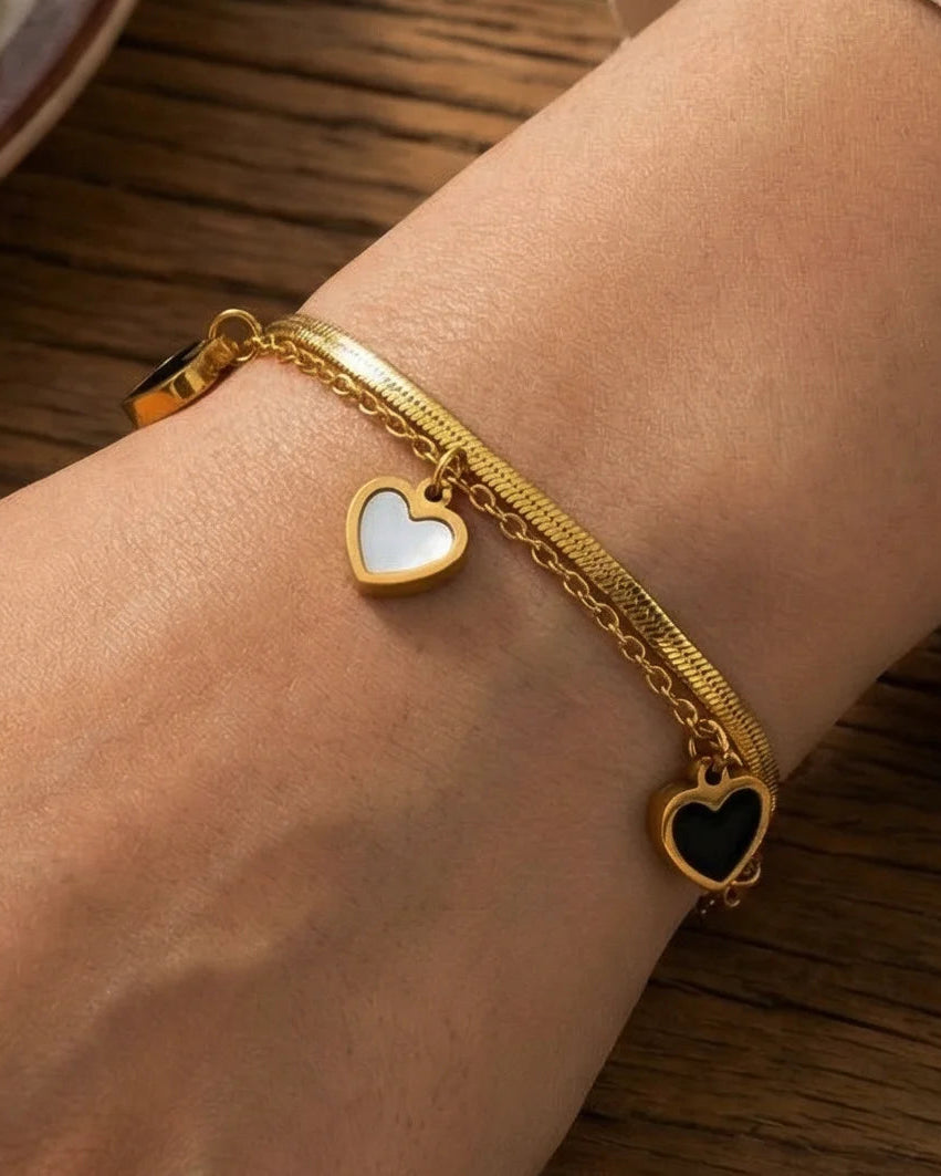 Zweilagiges Clara's Kontrast-Herzen Armband aus 18K vergoldetem Titanstahl mit drei schwarz-weißen Herzanhängern auf Marmorgrund