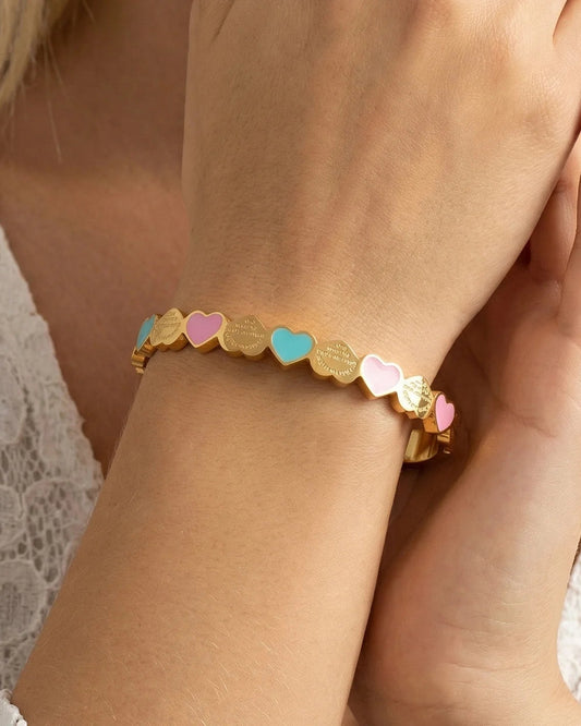 Gold-tone Lottie bangle with pink and green hearts worn on a wrist