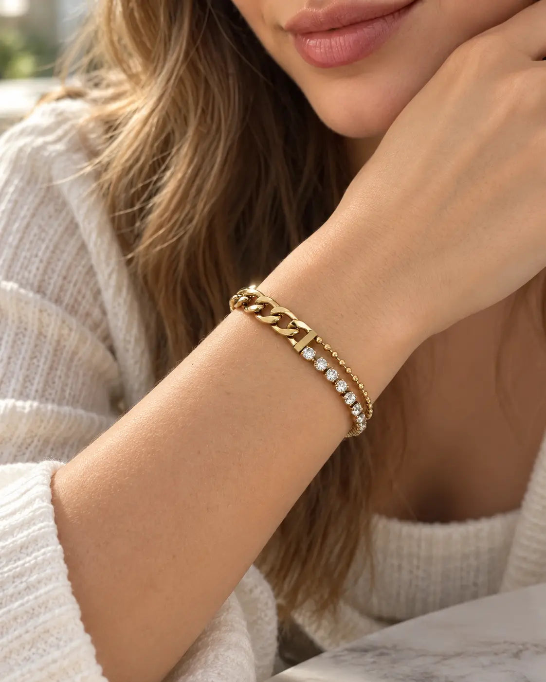 Frau im hellen Strickoberteil trägt das goldene Nerina Zirkonia Armband am angehobenen Handgelenk