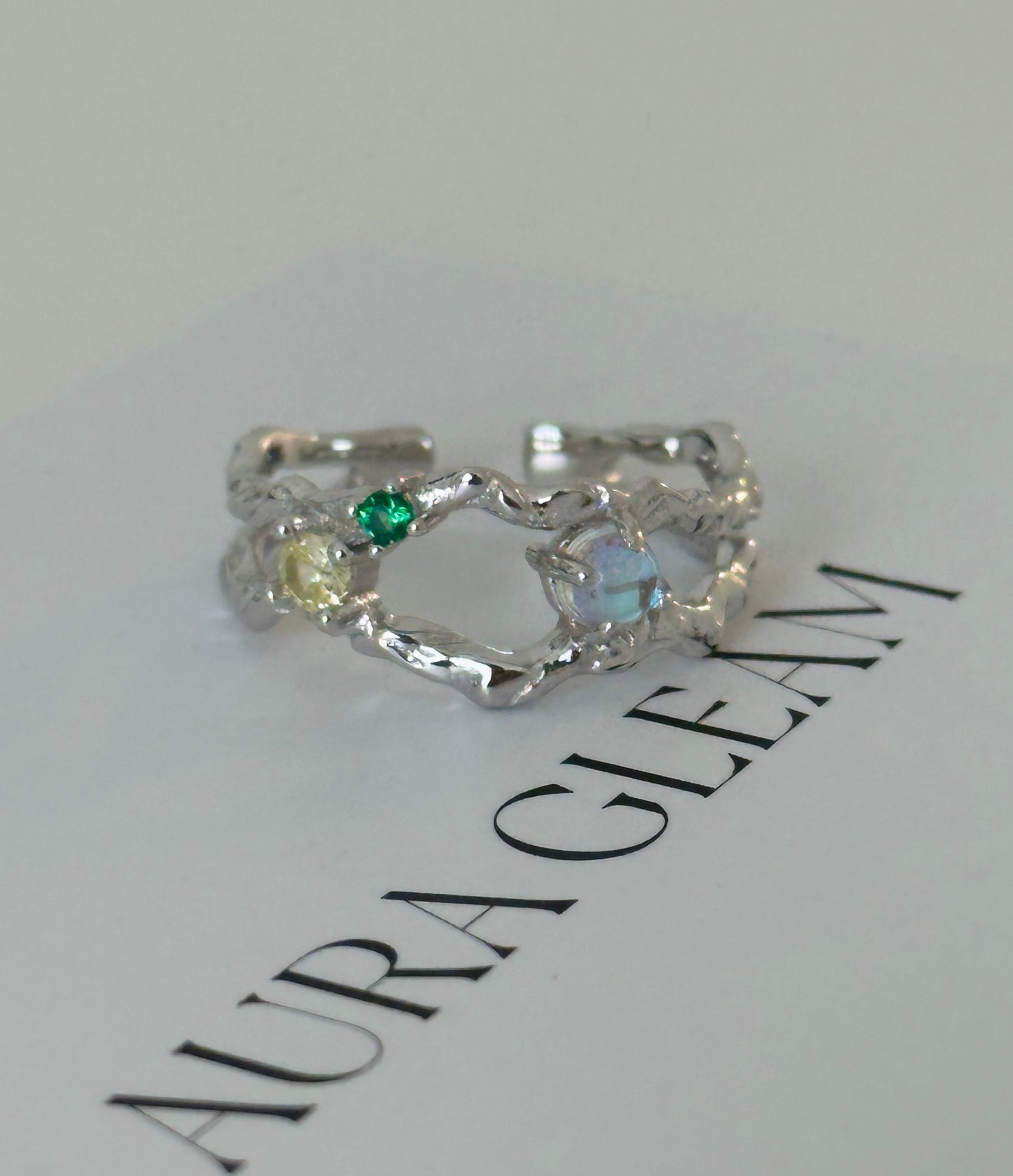 Offener Damenring aus 925er Silber mit leuchtendem Mondstein und bunten Zirkonia, präsentiert auf AURAGLEAM-Karte – elegantes, kunstvolles Design