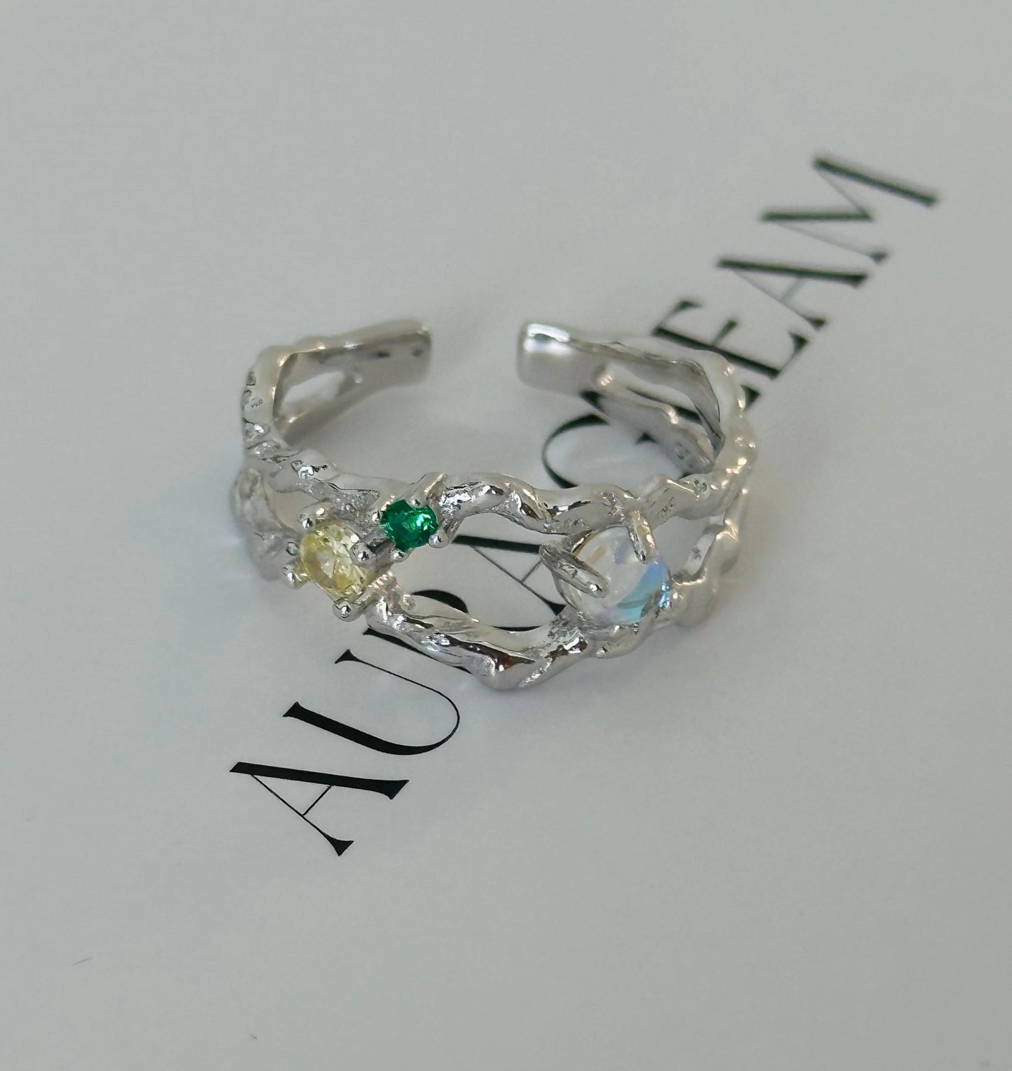 Offener Damenring aus 925er Silber mit leuchtendem Mondstein und bunten Zirkonia, präsentiert auf AURAGLEAM-Karte – elegantes, kunstvolles Design