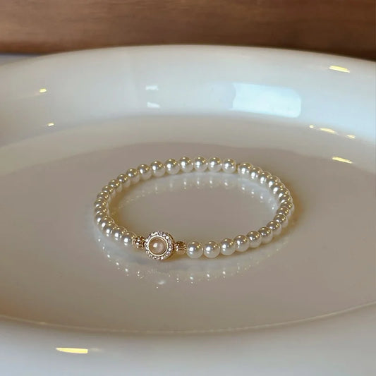 Klassisches Tessa's Schimmerndes Halo-Perlenarmband aus glänzenden Kunstperlen mit einem goldfarbenen Zirkonia-Mittelstück auf einem weißen Teller