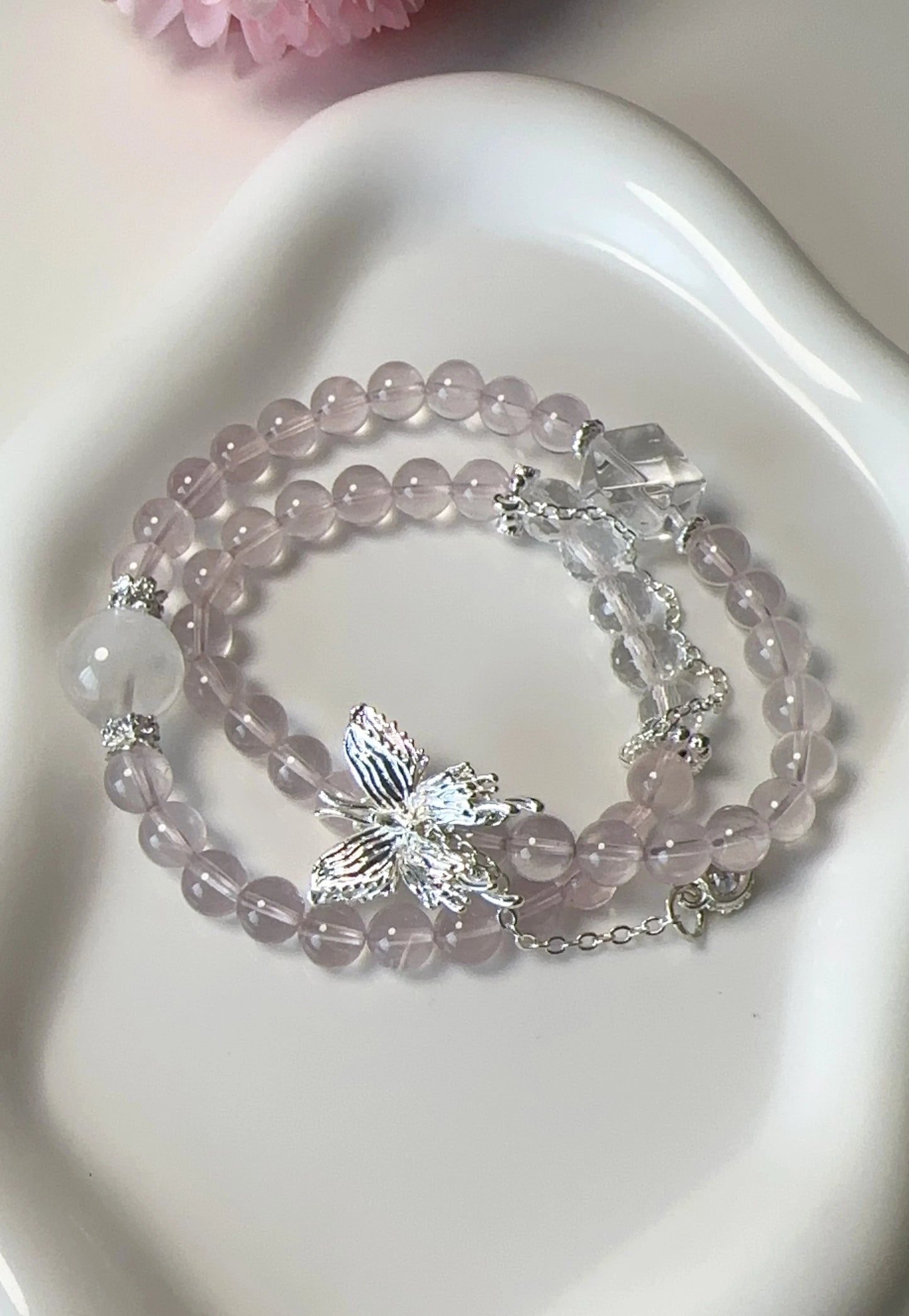 Rosa Rosenquarz-Perlenarmband mit Schmetterlingsanhänger – doppelt um den Finger gewickelt.