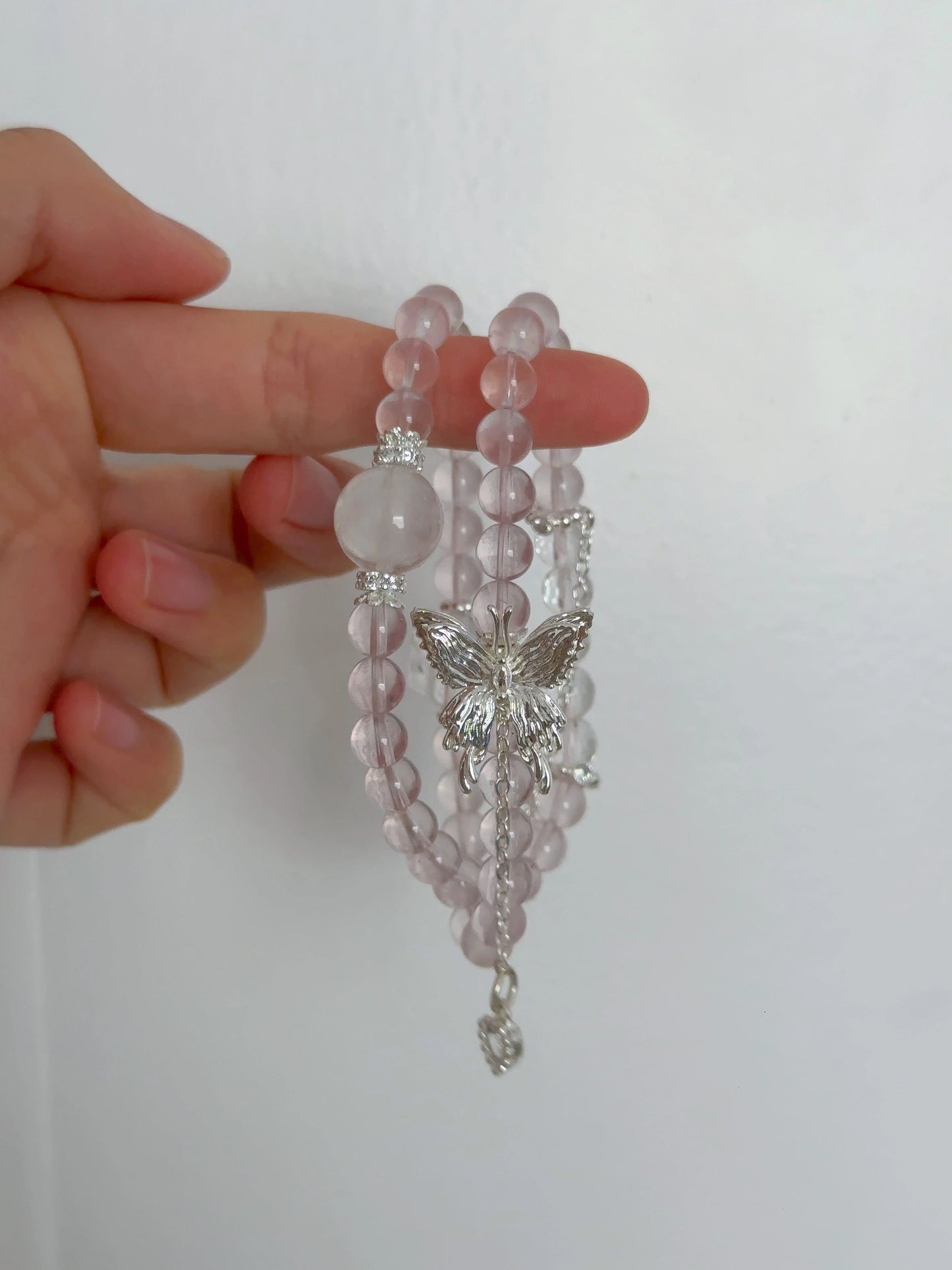 Rosa Rosenquarz-Perlenarmband mit Schmetterlingsanhänger – doppelt um den Finger gewickelt.