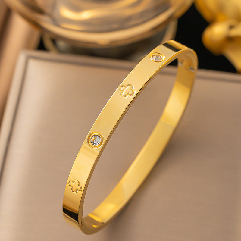 Vergoldeter Armreif mit Kleeblatt-Gravur und funkelnden Zirkonia-Steinen auf beigem Hintergrund