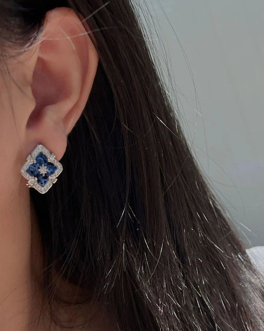 Vintage earring with a blue flower motif and pale sparkling surround worn on an ear