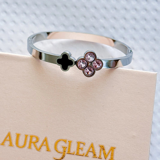 Silberfarbener Yuna's Funkelnder Glücksmoment Armreif aus Titanstahl mit einem rosa Zirkonia-Kleeblatt und einem schwarzen Emaille-Kleeblatt auf einer rosa Box