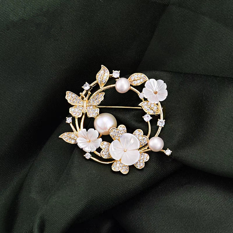 Elegante goldene Blumenkranz-Brosche mit Zirkoniablättern, geschnitzten Muschelblüten und rosa Süßwasserperlen – ideal für festliche Anlässe oder als Geschenk
