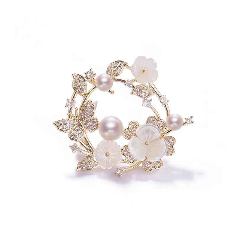 Elegante goldene Blumenkranz-Brosche mit Zirkoniablättern, geschnitzten Muschelblüten und rosa Süßwasserperlen – ideal für festliche Anlässe oder als Geschenk