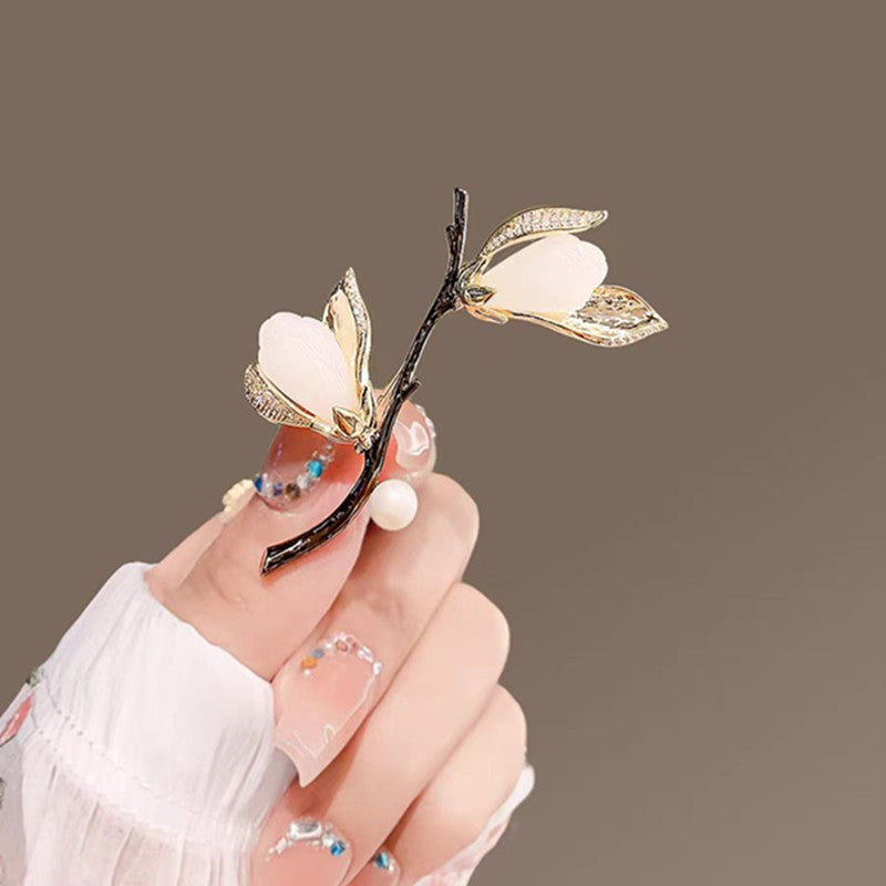 Elegante Magnolien-Brosche mit goldfarbenen Blütenblättern, Zirkoniabesatz und einer zarten Süßwasserperle – femininer Natur-Schmuck im asiatischen Stil
