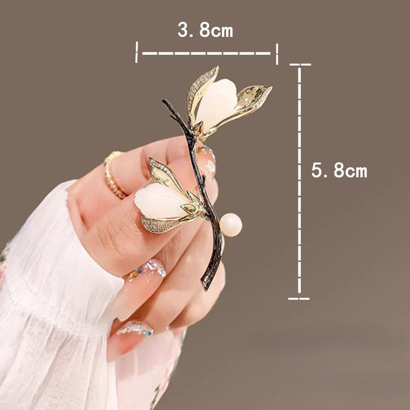 Elegante Magnolien-Brosche mit goldfarbenen Blütenblättern, Zirkoniabesatz und einer zarten Süßwasserperle – femininer Natur-Schmuck im asiatischen Stil