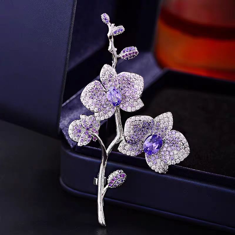 Elegante Orchideen-Brosche mit lila Zirkonia und Blütenmotiv auf silbernem Zweig