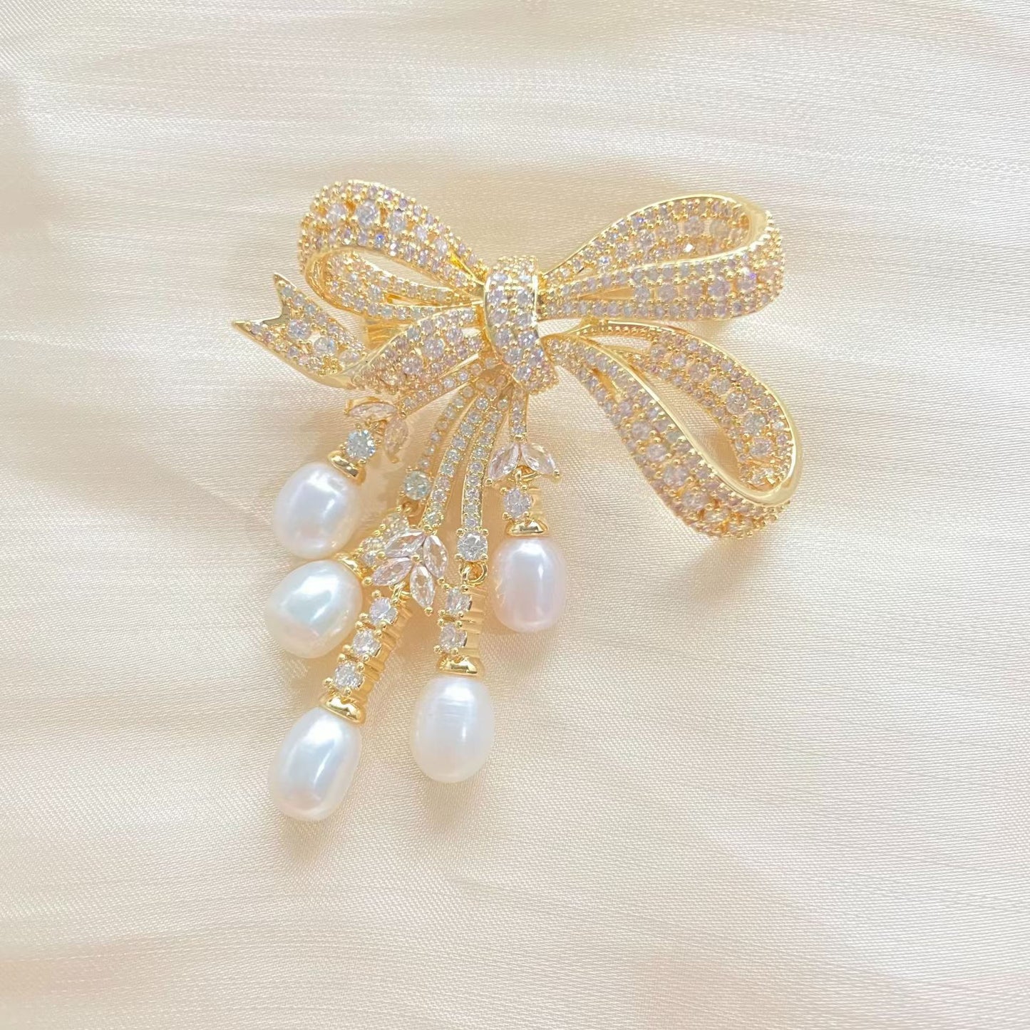 Goldene Schleifen-Brosche mit schimmernden Zirkonia und herabhängenden Süßwasserperlen – elegantes Design für festliche Anlässe