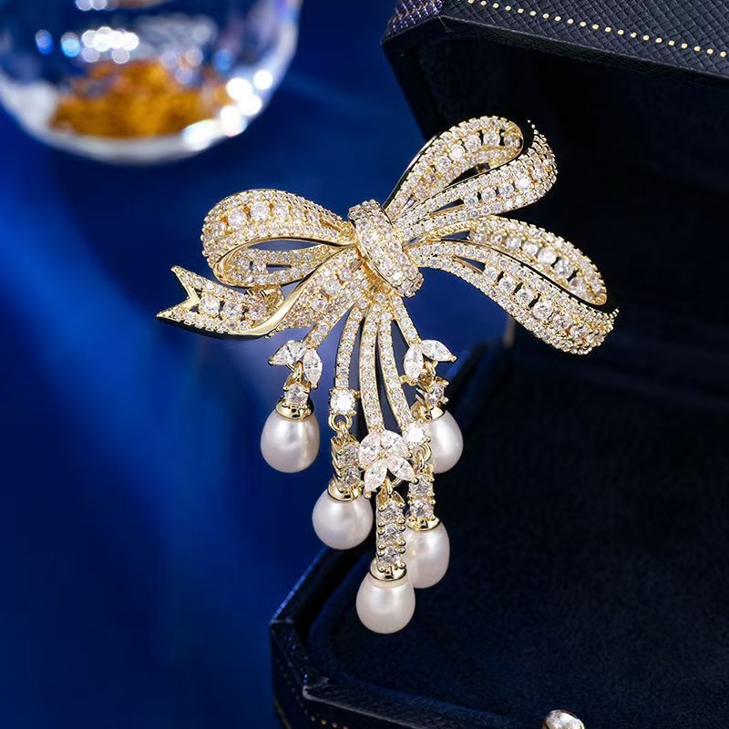 Goldene Schleifen-Brosche mit schimmernden Zirkonia und herabhängenden Süßwasserperlen – elegantes Design für festliche Anlässe