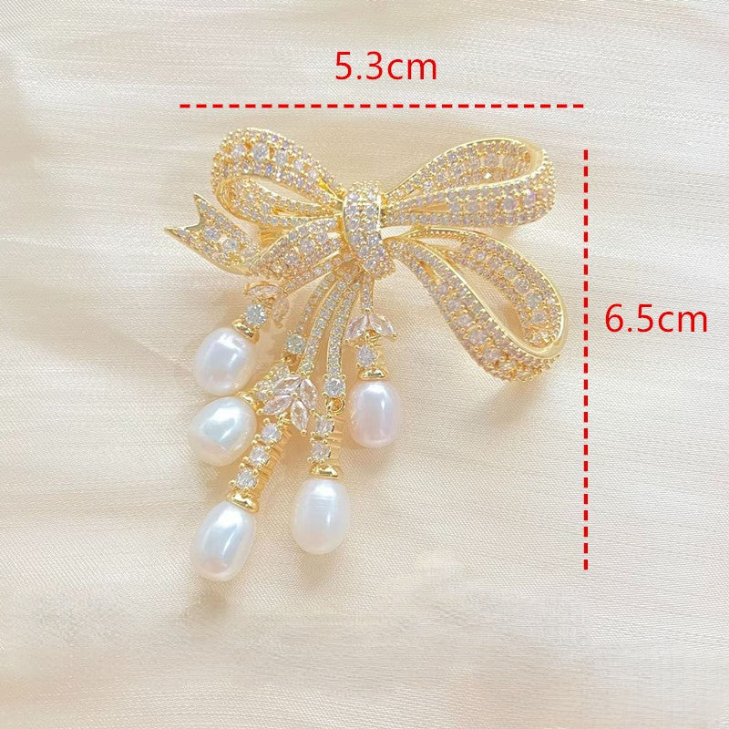 Goldene Schleifen-Brosche mit schimmernden Zirkonia und herabhängenden Süßwasserperlen – elegantes Design für festliche Anlässe