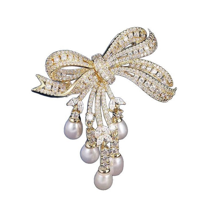 Goldene Schleifen-Brosche mit schimmernden Zirkonia und herabhängenden Süßwasserperlen – elegantes Design für festliche Anlässe