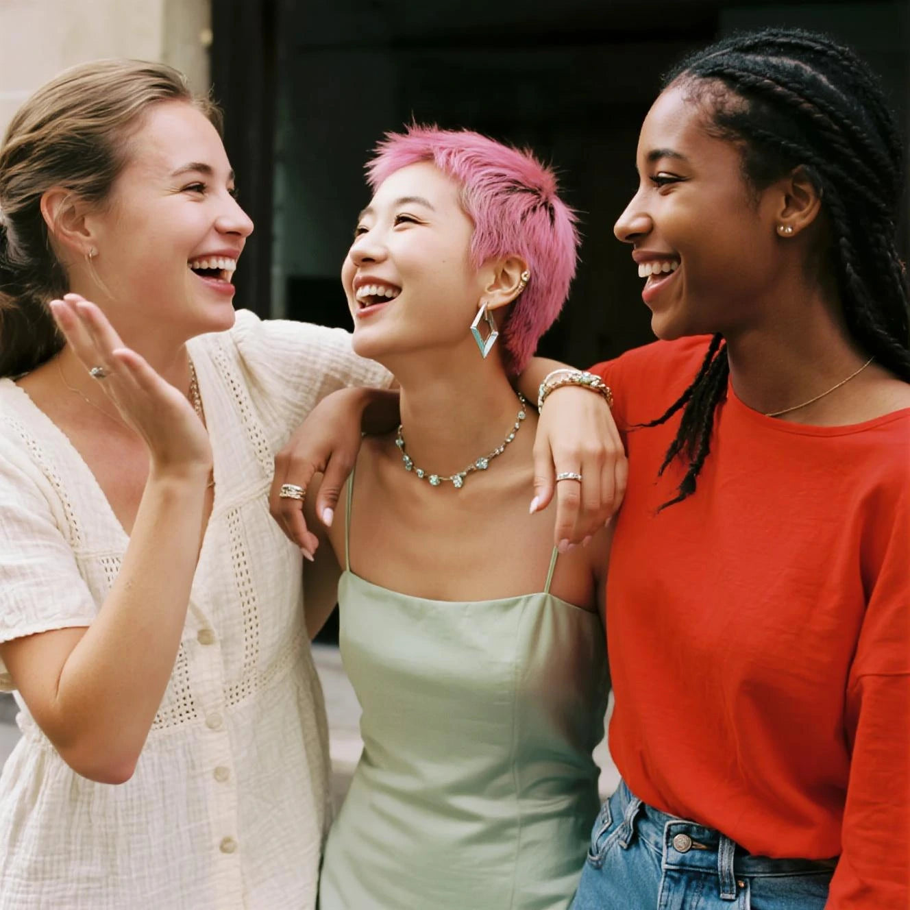 Drei fröhliche Frauen unterschiedlicher Herkunft tragen stilvollen Schmuck und lachen gemeinsam