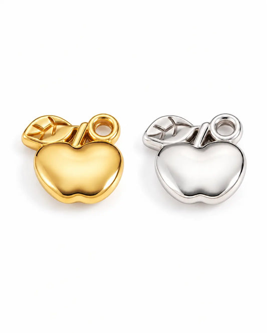 Alma Apfel Charms in Gold und Silber aus Edelstahl mit glänzender Apfelform und strukturiertem Blatt auf Weiß