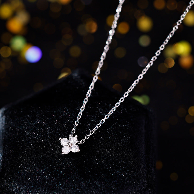 Feine Silberkette mit funkelndem Blütenanhänger aus vier Zirkonia-Steinen auf schwarzem Hintergrund.