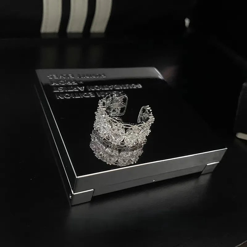 Breiter silberner Ring mit funkelnden Zirkonia Steinen in Blütenform auf schwarzem Hintergrund