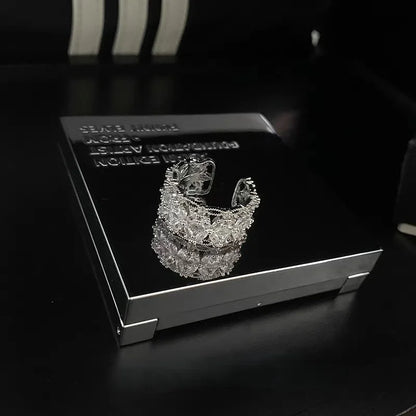 Breiter silberner Ring mit funkelnden Zirkonia Steinen in Blütenform auf schwarzem Hintergrund