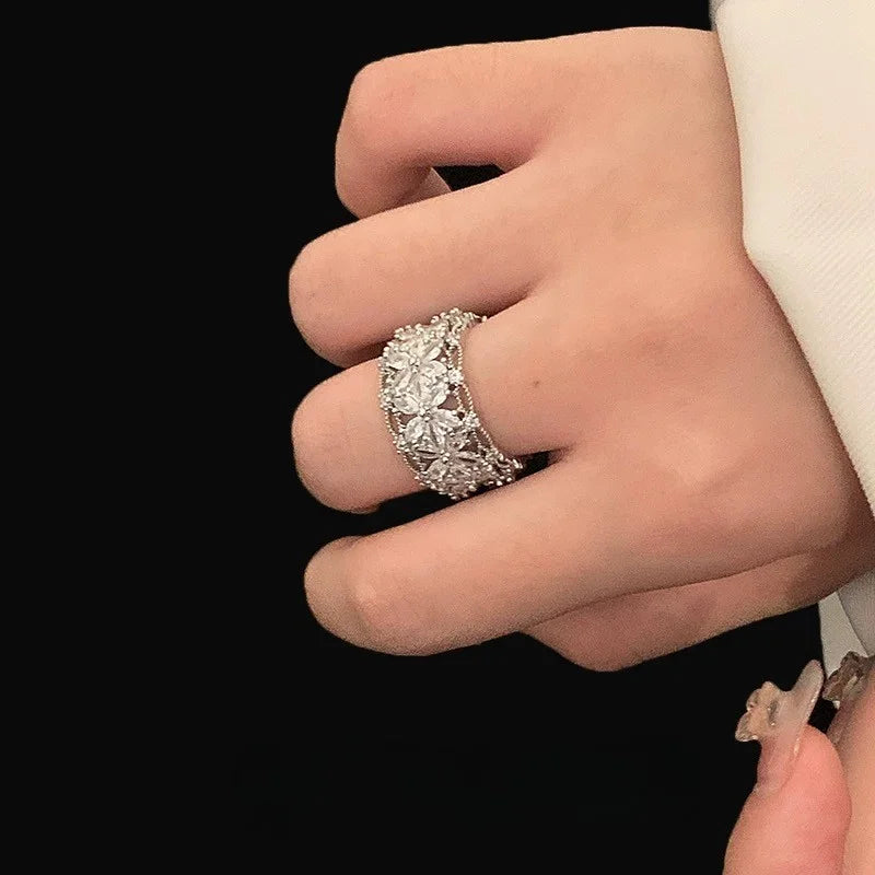 Breiter silberner Ring mit funkelnden Zirkonia Steinen in Blütenform auf schwarzem Hintergrund