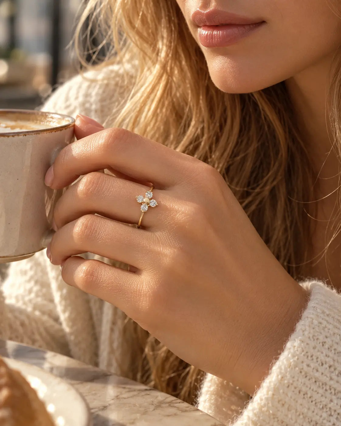 Frau im hellen Strickoberteil hält eine Tasse und trägt den goldenen Elina Zirkonia Blumenring