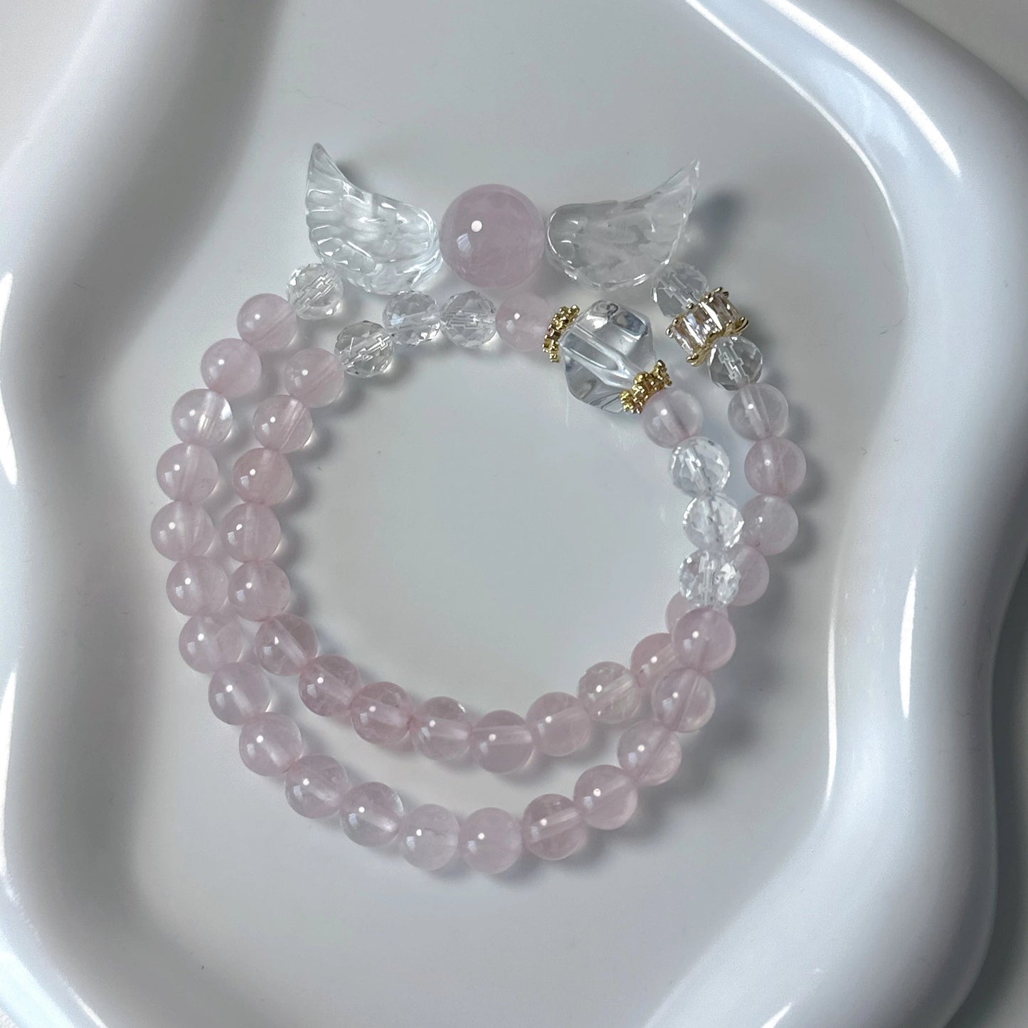 Doppellagiges Armband mit Rosenquarz, Bergkristall und Engelsflügel-Anhänger auf weißem Teller – zart und spirituell