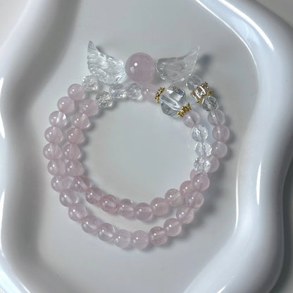 Doppellagiges Armband mit Rosenquarz, Bergkristall und Engelsflügel-Anhänger auf weißem Teller – zart und spirituell