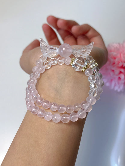 Doppellagiges Armband mit Rosenquarz, Bergkristall und Engelsflügel-Anhänger auf weißem Teller – zart und spirituell