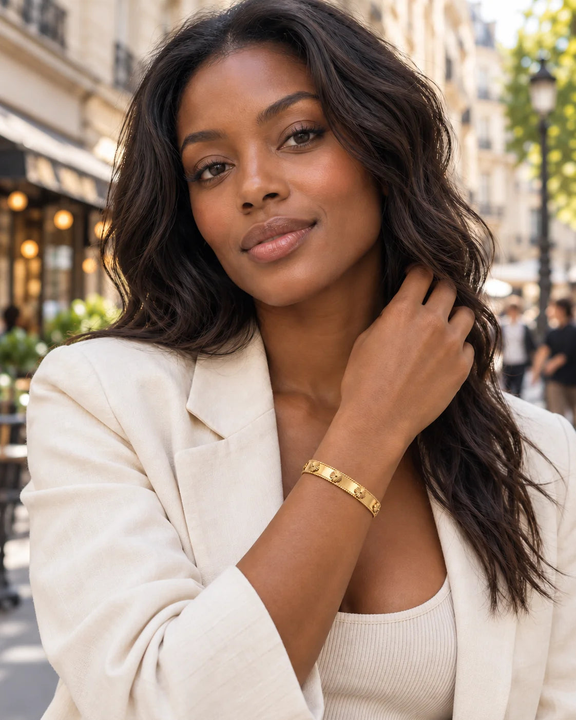 Goldfarbener Flora Armreif am Handgelenk eines Models mit hellem Blazer im Freien