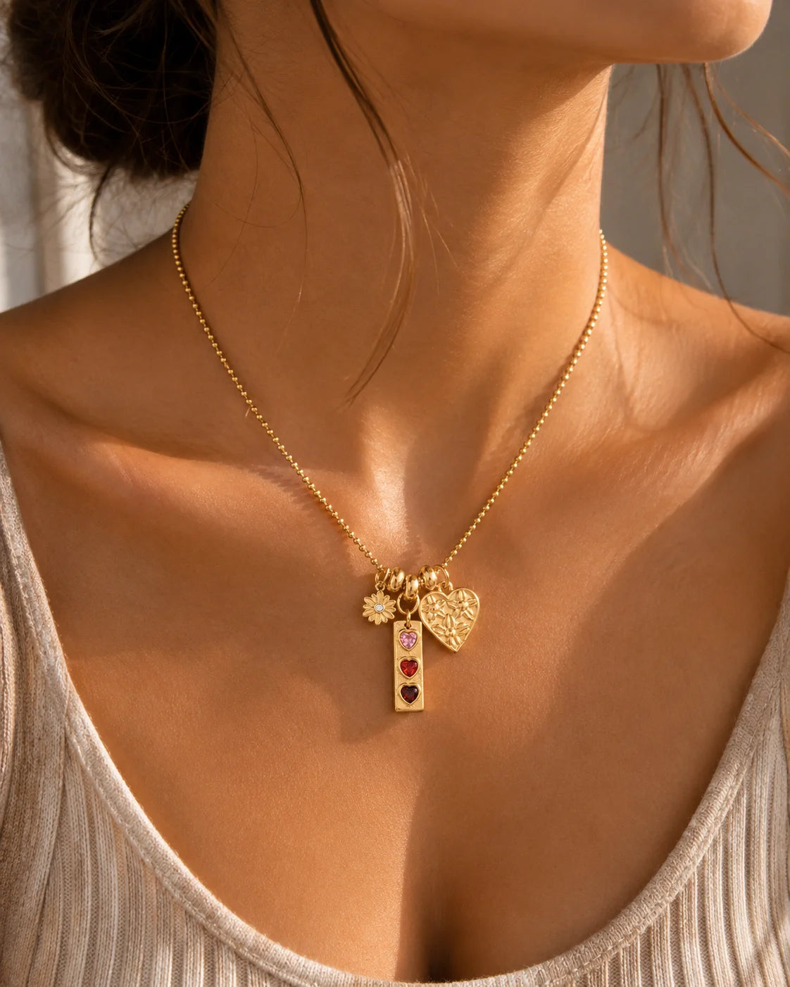 Goldene Kugelkette aus 18K vergoldetem Titanstahl mit drei verschiedenen Anhängern: einer Blume, einem länglichen Anhänger mit drei bunten Herzsteinen und einem geprägten Herz.