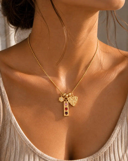 Goldene Kugelkette aus 18K vergoldetem Titanstahl mit drei verschiedenen Anhängern: einer Blume, einem länglichen Anhänger mit drei bunten Herzsteinen und einem geprägten Herz.