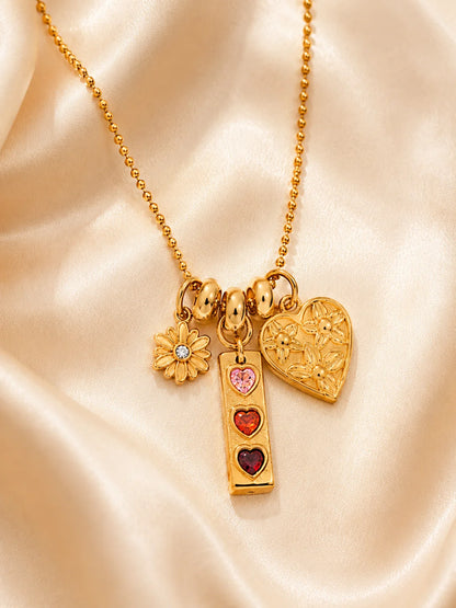 Goldene Kugelkette aus 18K vergoldetem Titanstahl mit drei verschiedenen Anhängern: einer Blume, einem länglichen Anhänger mit drei bunten Herzsteinen und einem geprägten Herz.