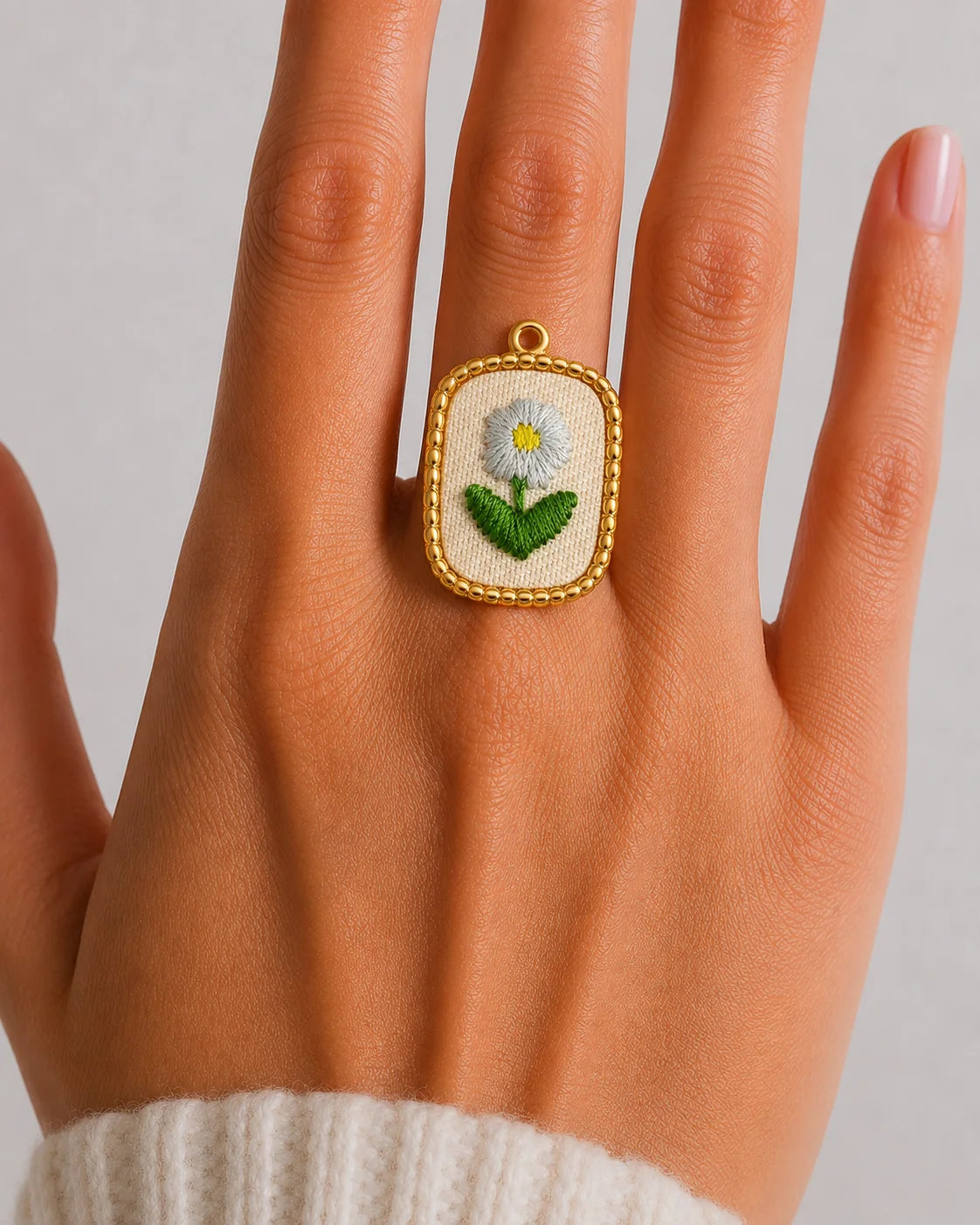 Ovaler, goldener Anhänger aus 18K vergoldetem Titanstahl mit Kugelbordüre und einem textilen Inlay, auf dem eine weiße Margerite gestickt ist, für personalisierbare Armbänder und Ketten