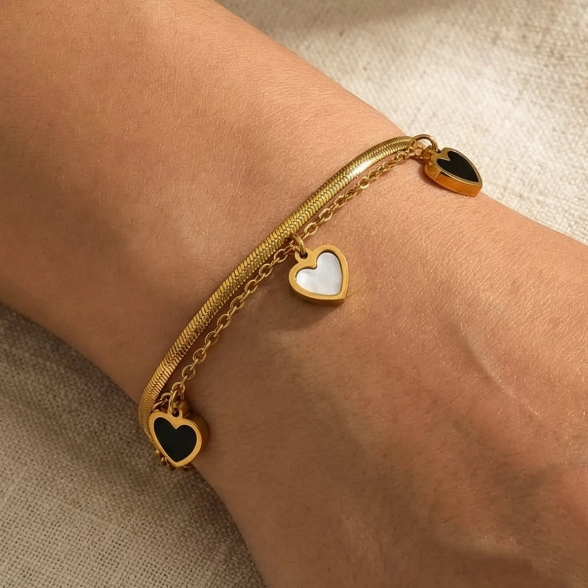 Zweilagiges Clara's Kontrast-Herzen Armband aus 18K vergoldetem Titanstahl mit drei schwarz-weißen Herzanhängern auf Marmorgrund