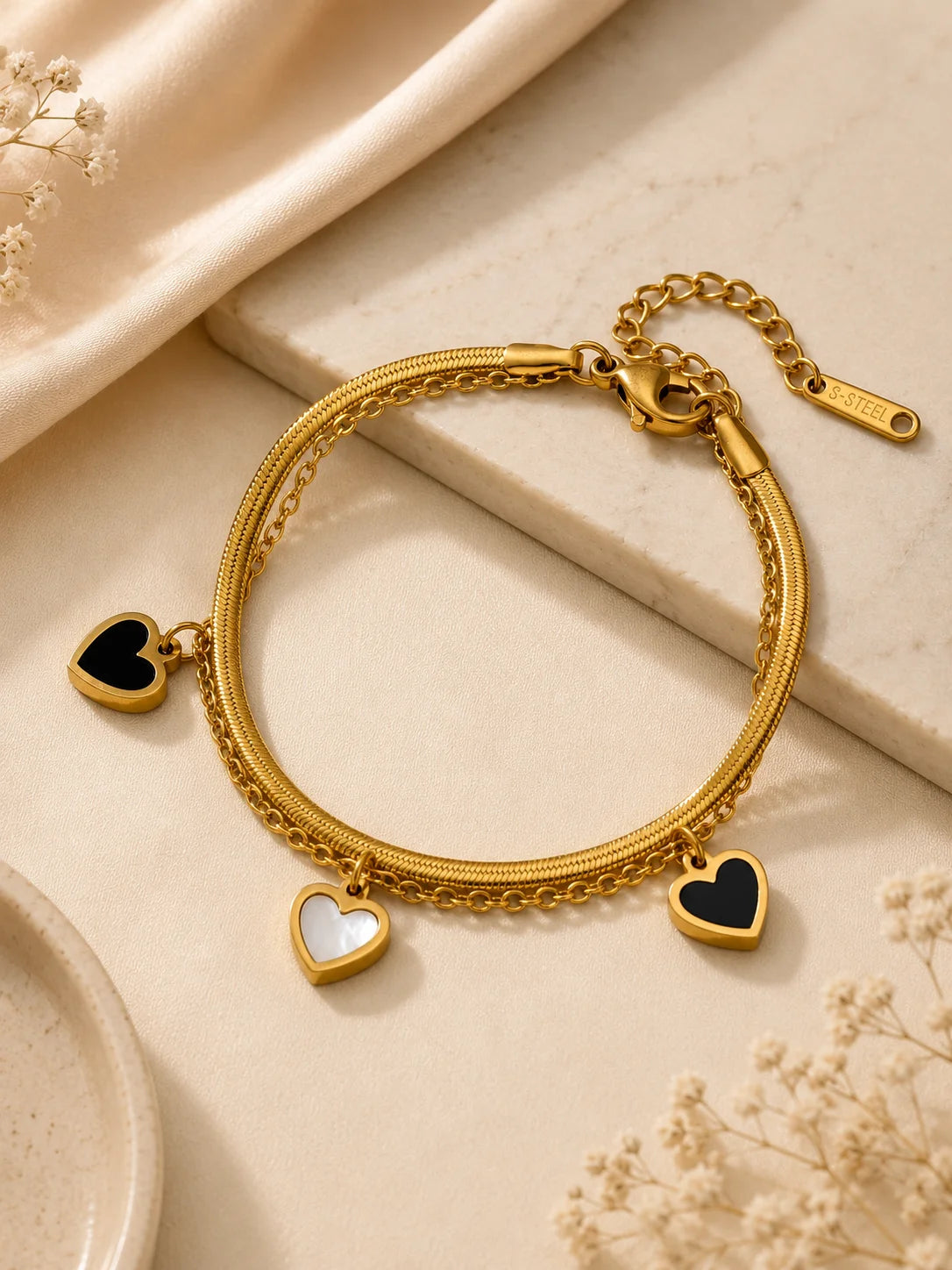 Zweilagiges Clara's Kontrast-Herzen Armband aus 18K vergoldetem Titanstahl mit drei schwarz-weißen Herzanhängern auf Marmorgrund