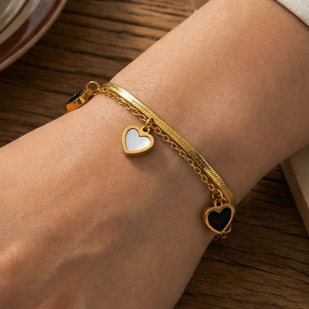 Zweilagiges Clara's Kontrast-Herzen Armband aus 18K vergoldetem Titanstahl mit drei schwarz-weißen Herzanhängern auf Marmorgrund