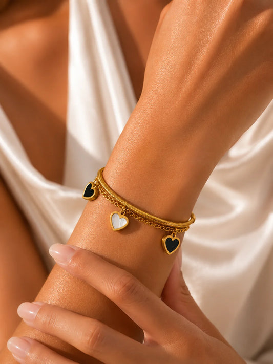 Zweilagiges Clara's Kontrast-Herzen Armband aus 18K vergoldetem Titanstahl mit drei schwarz-weißen Herzanhängern auf Marmorgrund