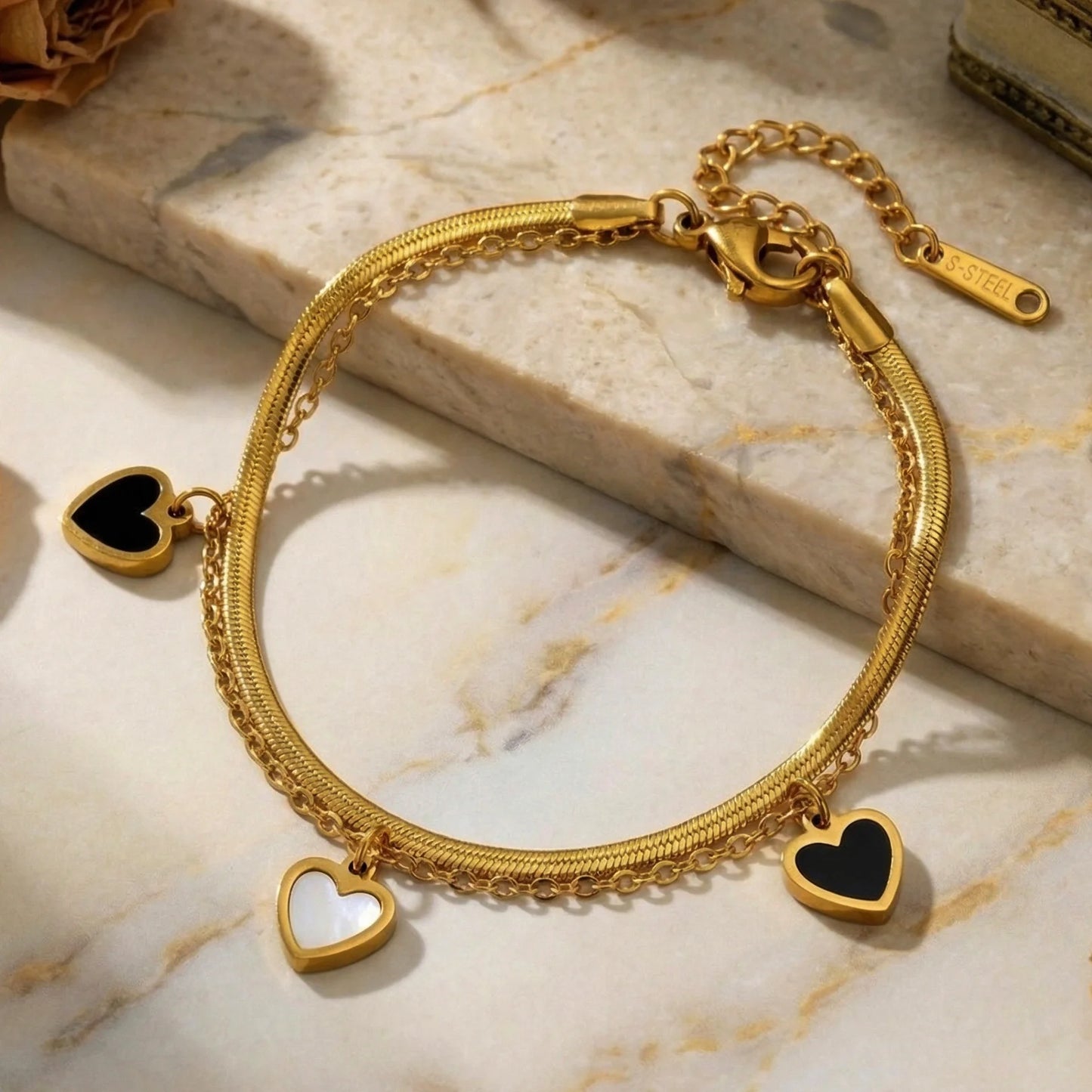 Zweilagiges Clara's Kontrast-Herzen Armband aus 18K vergoldetem Titanstahl mit drei schwarz-weißen Herzanhängern auf Marmorgrund