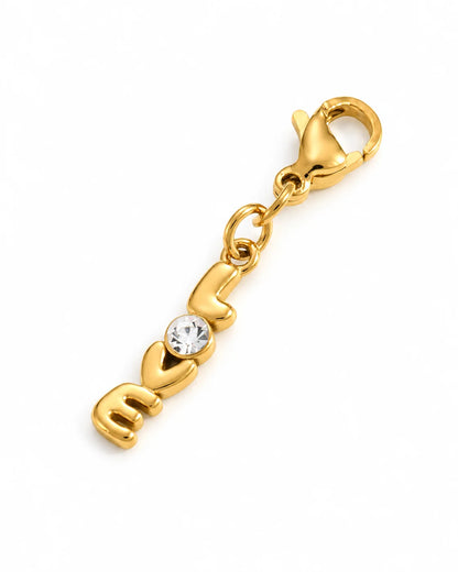 Goldener LOVE Charm aus 18K-vergoldetem Edelstahl mit Herz, klarem Schmuckstein und Karabinerverschluss auf weißem Hintergrund
