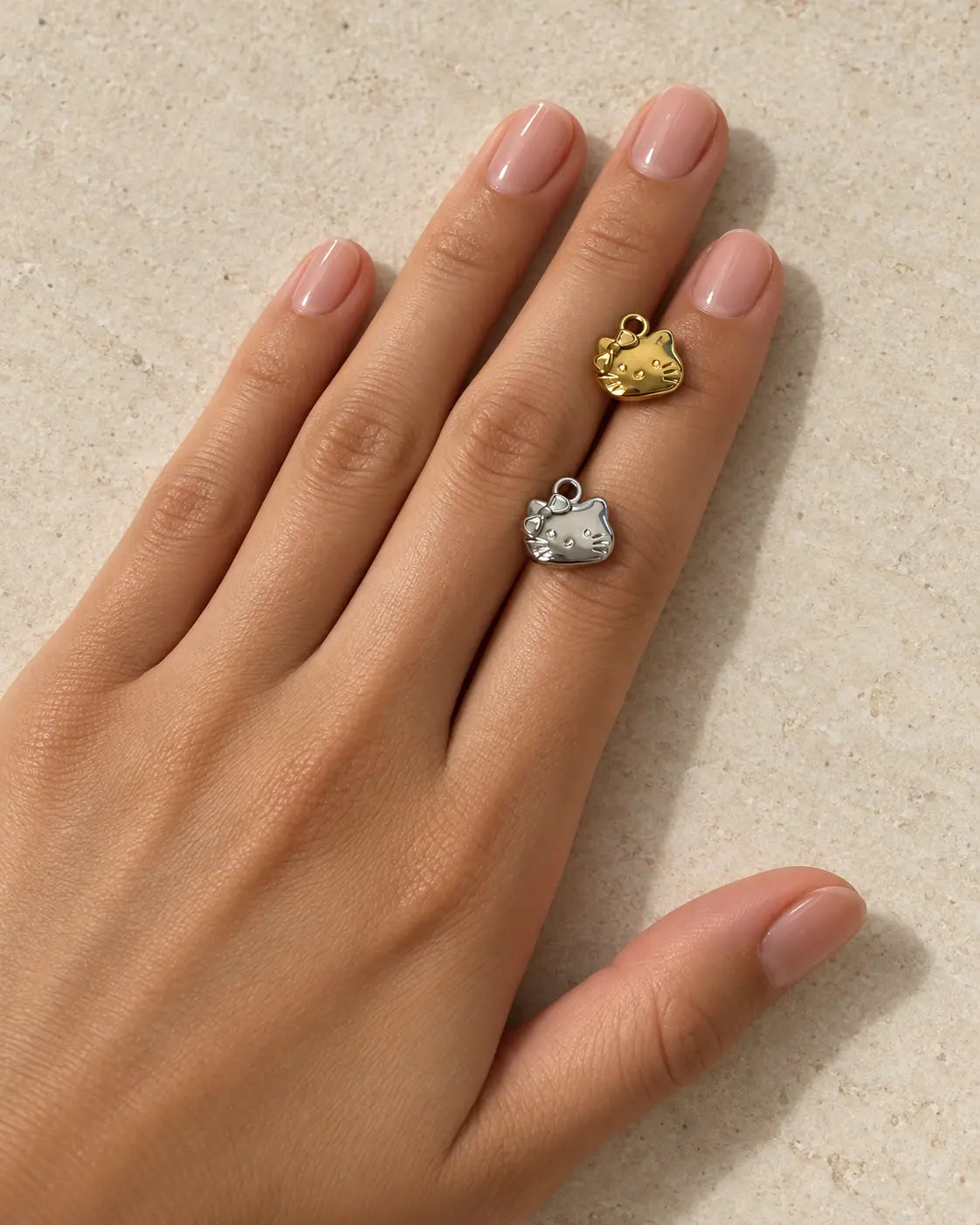 Goldener und silberfarbener Mimi Katzen Charm auf einer Hand vor hellem Steinhintergrund