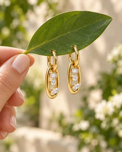 Ovale goldene Zirkonia Ohrhänger auf grünem Blatt präsentiert