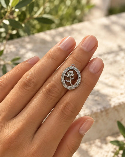 Silberfarbener Rosalie Rosen Charm auf einer Hand vor einem Garten, Detailansicht des durchbrochenen Rosenmotivs