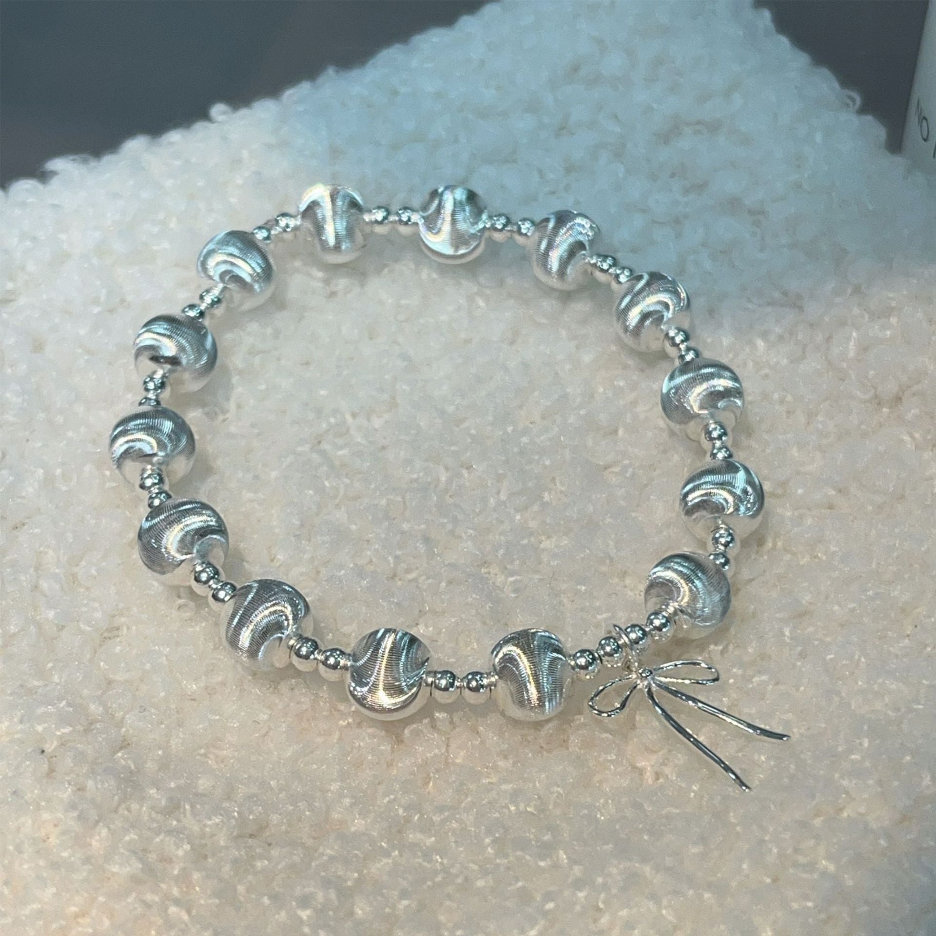 Handgefertigtes Armband aus 925er Silber mit schimmernden Katzenaugenperlen und Schleifenanhänger – elegant und verspielt