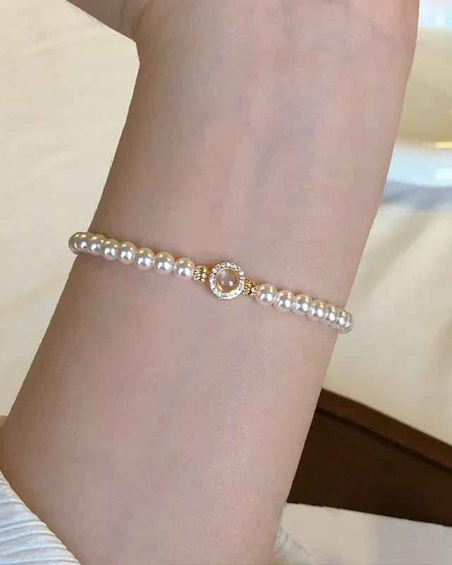 Klassisches Tessa's Schimmerndes Halo-Perlenarmband aus glänzenden Kunstperlen mit einem goldfarbenen Zirkonia-Mittelstück auf einem weißen Teller