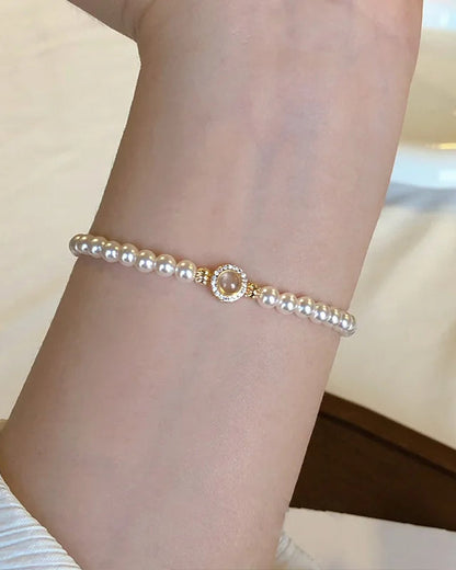 Klassisches Tessa's Schimmerndes Halo-Perlenarmband aus glänzenden Kunstperlen mit einem goldfarbenen Zirkonia-Mittelstück auf einem weißen Teller